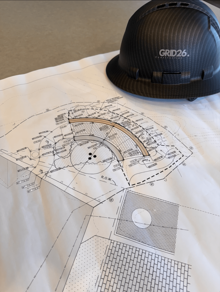 A GRID26 branded hardhat sitting on the blueprints for a construction project.
